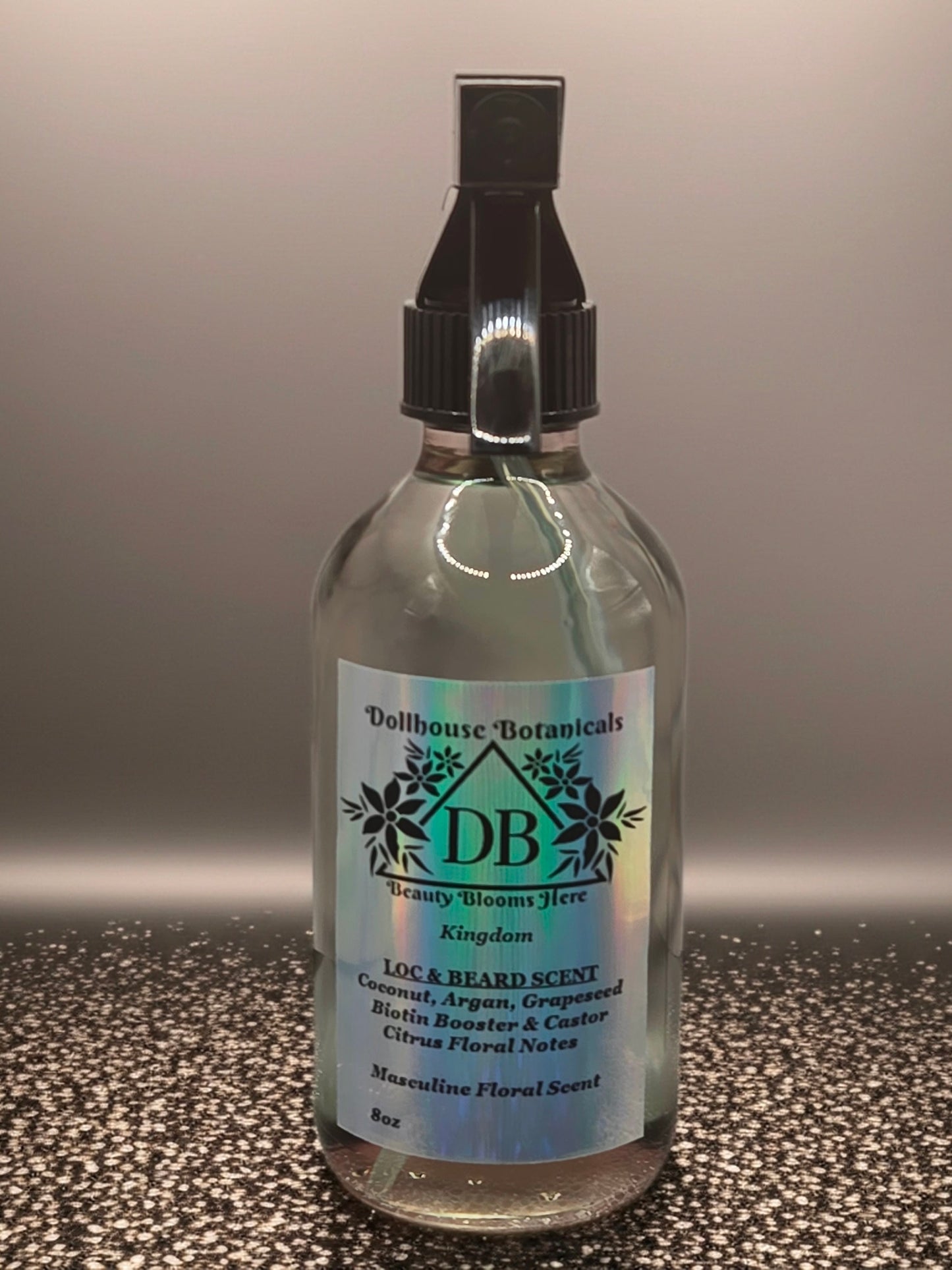 Bottle of Dollhouse Botanicals Kingdom Loc and Beard Scent. Oil in glass bottle with trigger sprayer. Front facing with label and ingredients displayed.