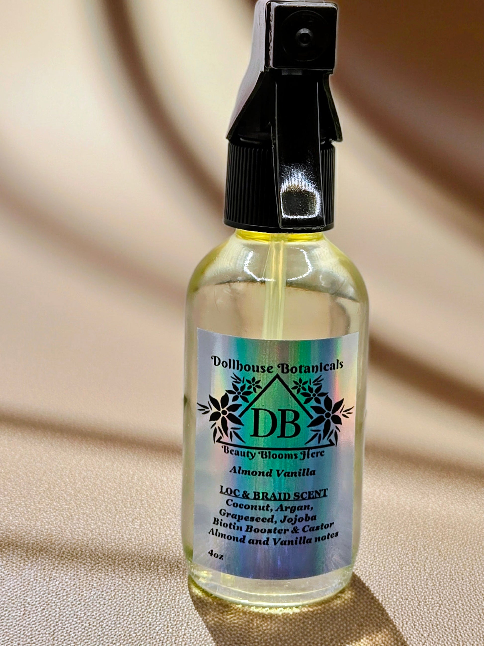 Bottle of Dollhouse Botanicals Almond Vanilla Loc and Braid Scent. Oil in clear glass bottle with black trigger sprayer applicator. Feminine hair fragrance.