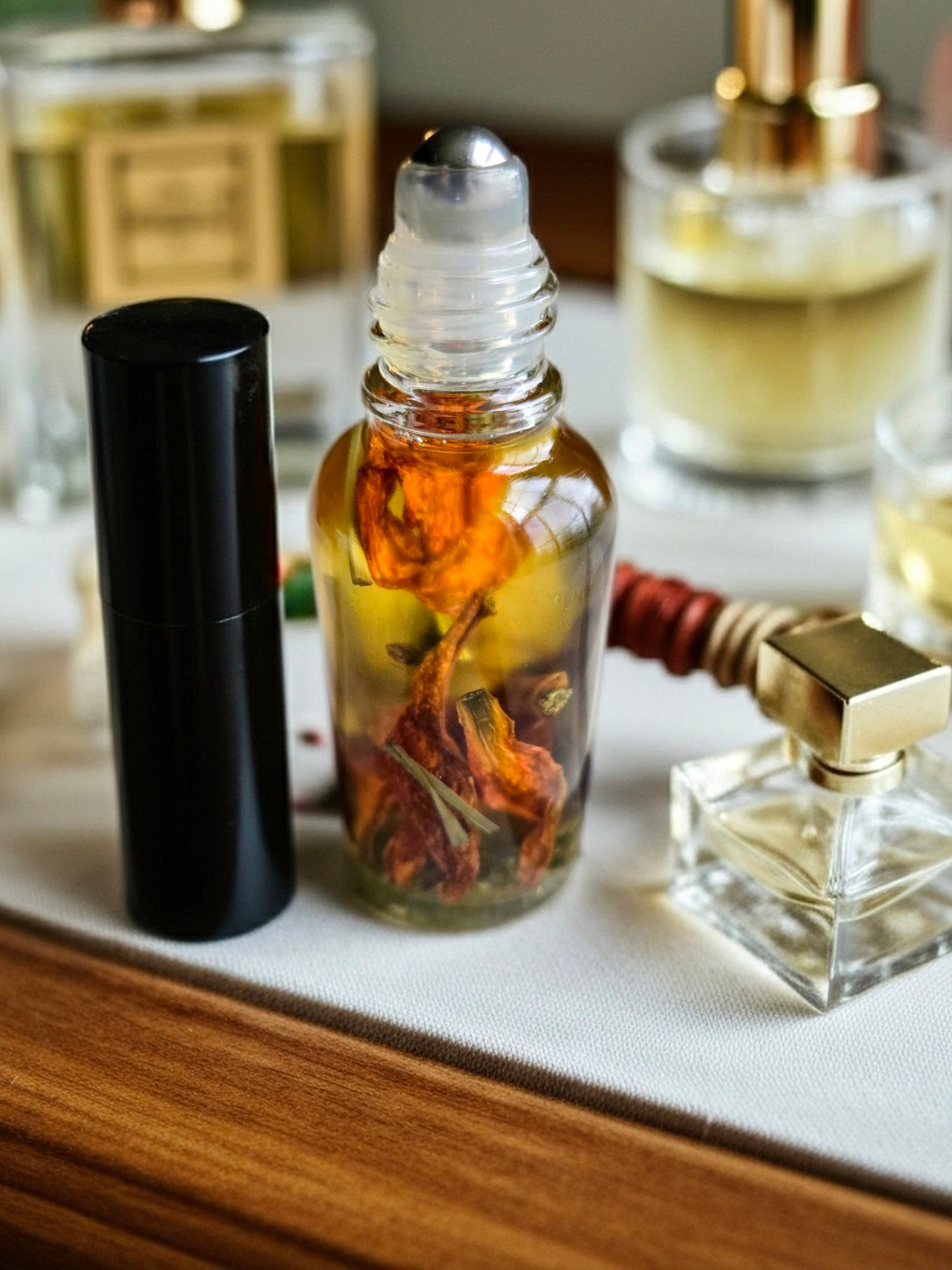 Bottle of Dollhouse Botanicals Bohemia Flora Face Hydrator. Golden oil with floating lemongrass and orange lily in glass bottle with steel roller ball applicator.