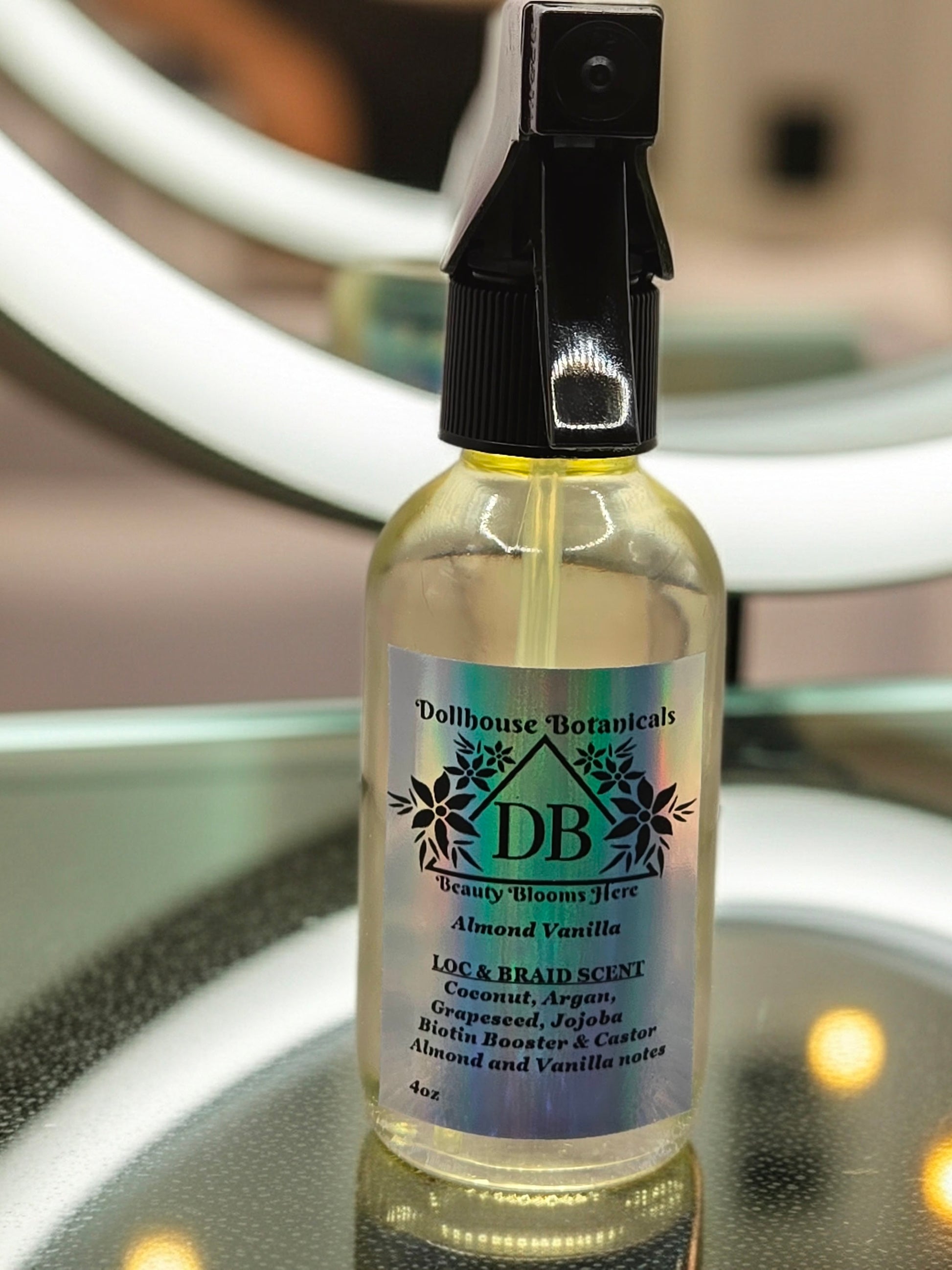 Bottle of Dollhouse Botanicals Loc and Braid Scent. Oil in clear glass bottle with black trigger sprayer applicator. Feminine hair fragrance.