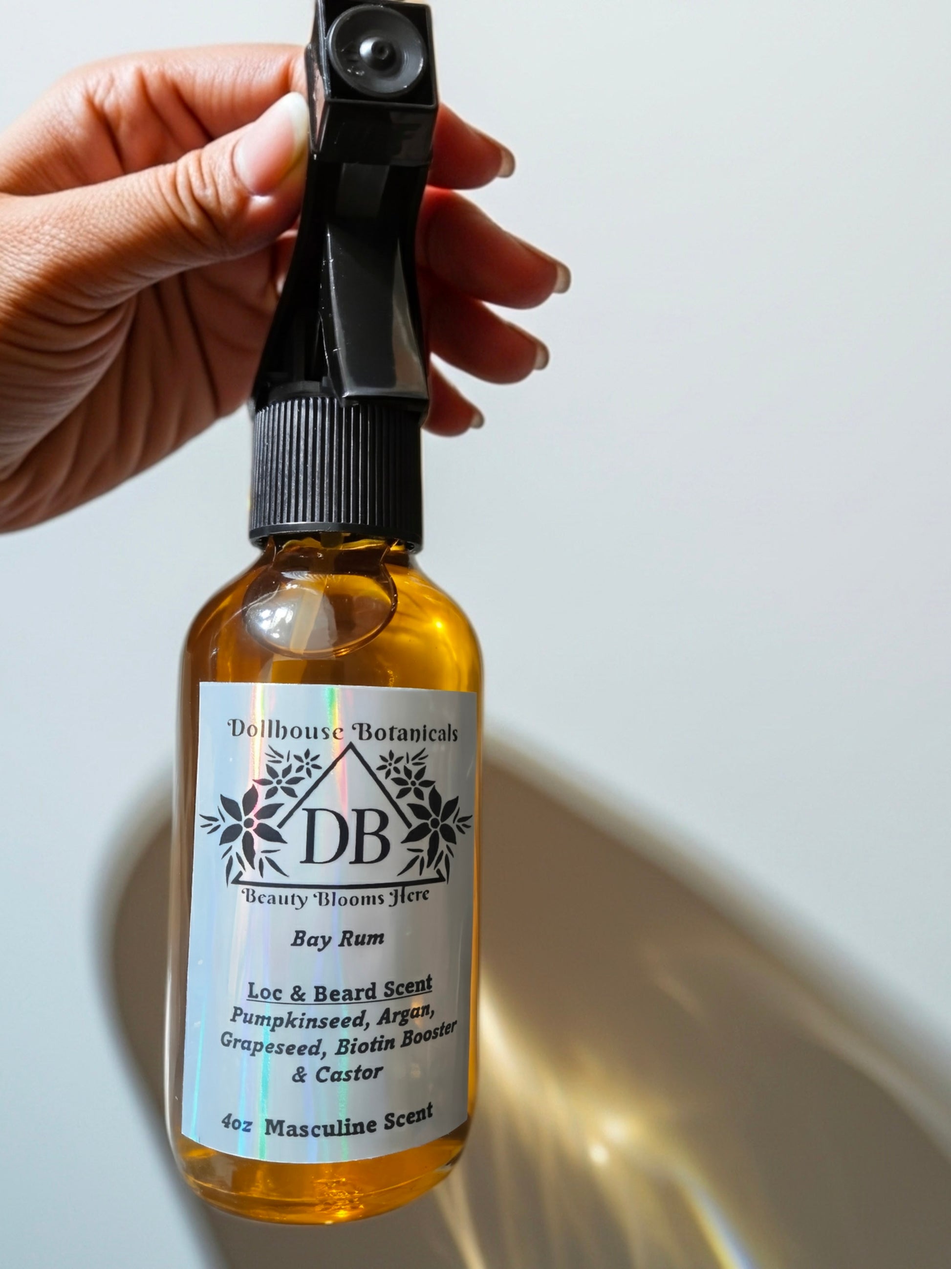 Bottle of Dollhouse Botanicals Bay Rum Loc and Beard Scent. Golden oil in glass bottle. Front facing with label and ingredients displayed, held in hand.