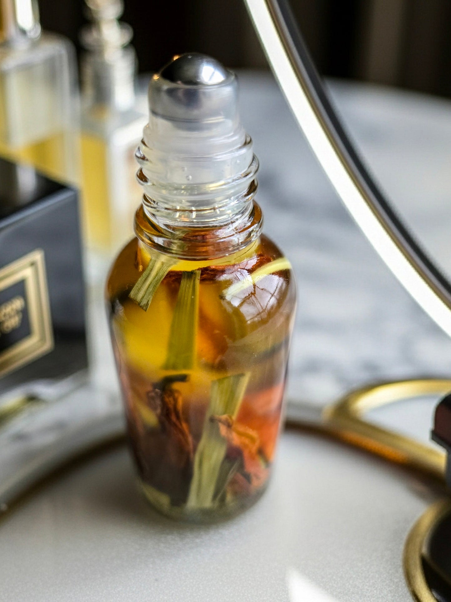 Bottle of Dollhouse Botanicals Bohemia Flora Face Hydrator. Golden oil with floating lemongrass and orange lily in glass bottle with steel roller ball applicator.