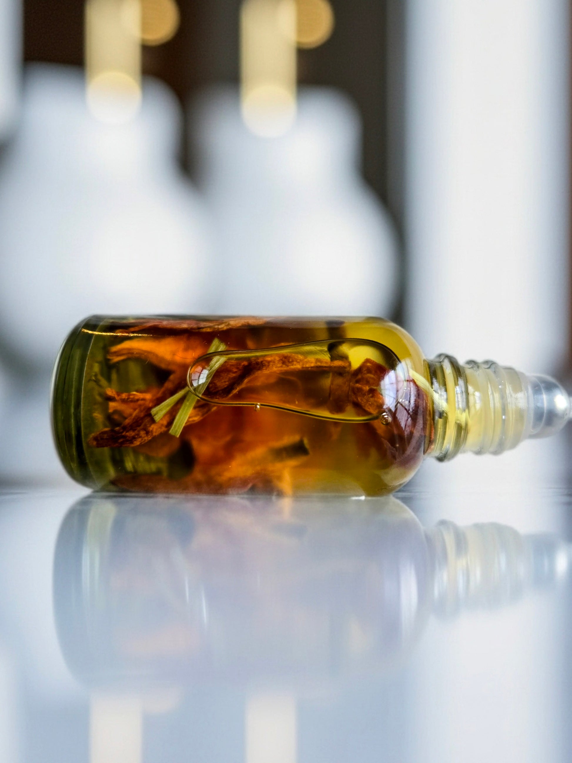 Bottle of Dollhouse Botanicals Bohemia Flora Face Hydrator. Golden oil with floating lemongrass and orange lily in glass bottle with steel roller ball applicator.