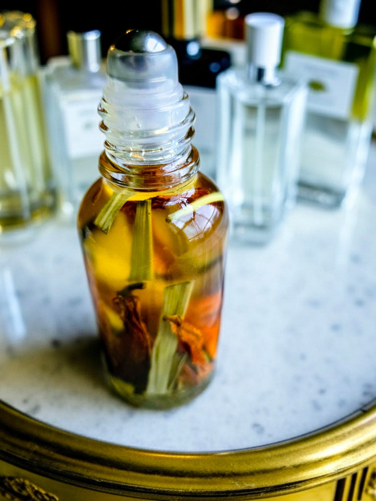  Bottle of Dollhouse Botanicals Bohemia Flora Face Hydrator. Golden oil with floating lemongrass and orange lily in glass bottle with steel roller ball applicator.