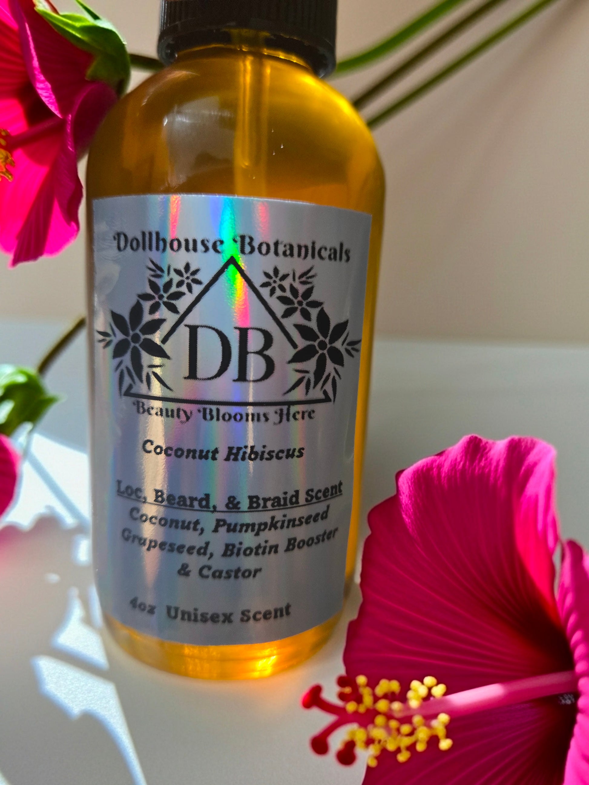 Bottle of Dollhouse Botanicals Coconut Hibiscus Loc, Beard, and Braid Scent. Golden oil in glass bottle. Front facing with label and ingredients displayed. Unisex hair fragrance.