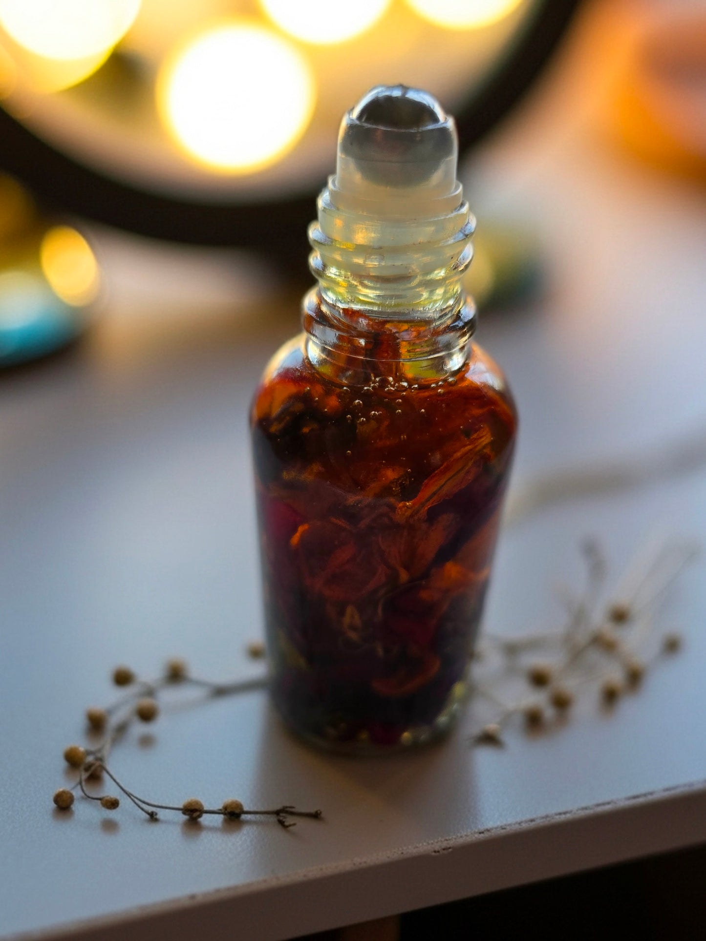 Bottle of Dollhouse Botanicals Deity Flora Face Hydrator. Golden oil with floating orange lily, purple myosotis and crushed Chines rose petals in glass bottle with steel roller ball applicator.