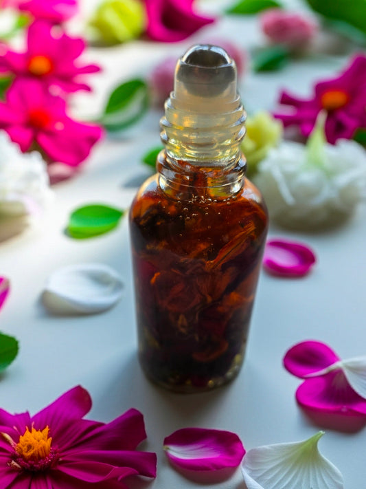 Bottle of Dollhouse Botanicals Deity Flora Face Hydrator. Botanicals floating in reddish gold oil in bottle with steel roll on applicator.