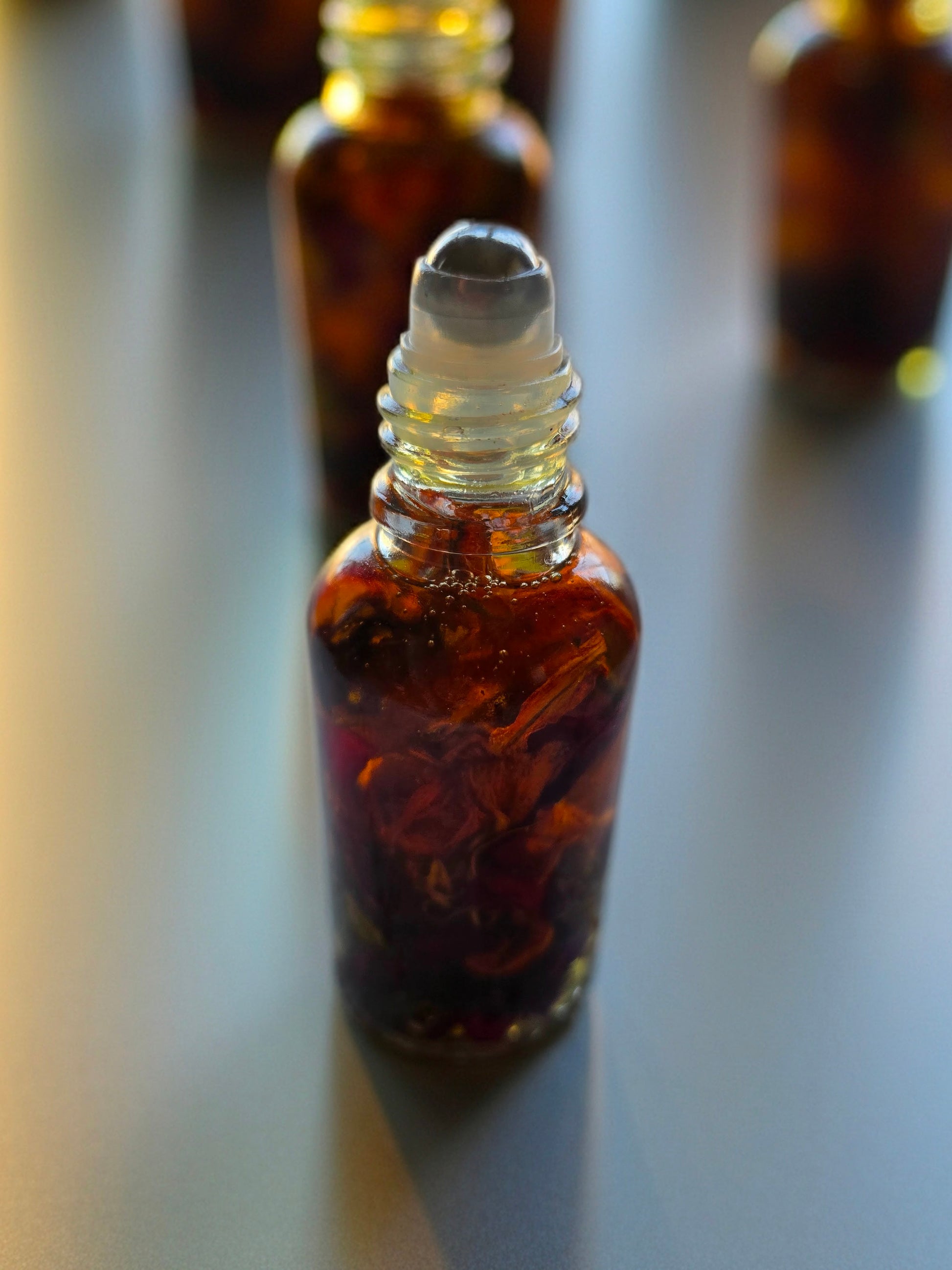 Bottle of Dollhouse Botanicals Deity Flora Face Hydrator. Golden oil with floating orange lily, purple myosotis and crushed Chines rose petals in glass bottle with steel roller ball applicator.