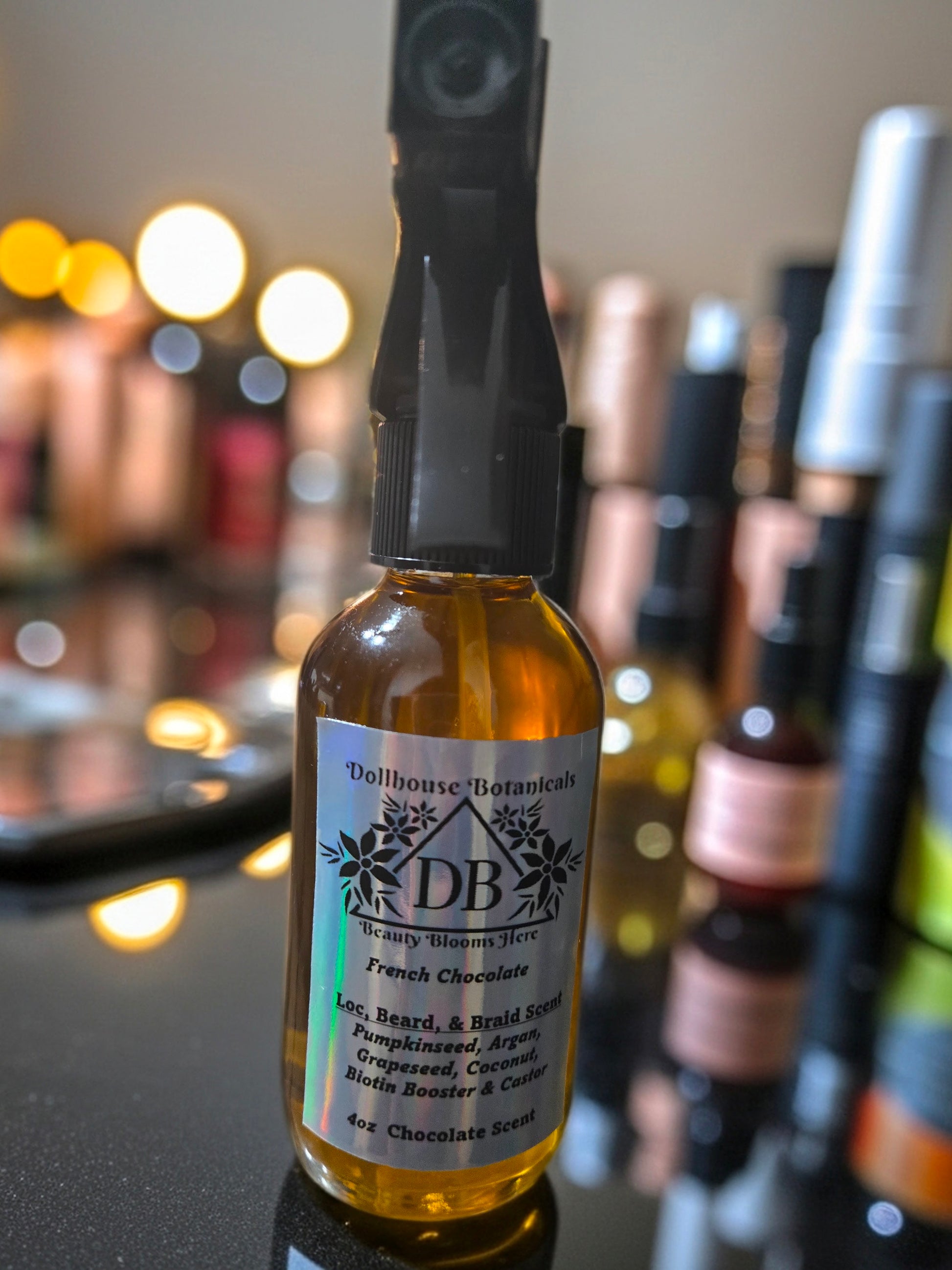  Bottle of Dollhouse Botanicals French Chocolate Loc, Beard, and Braid Scent. Golden oil in glass bottle with trigger sprayer. Front facing with label and ingredients displayed. Unisex hair scent.