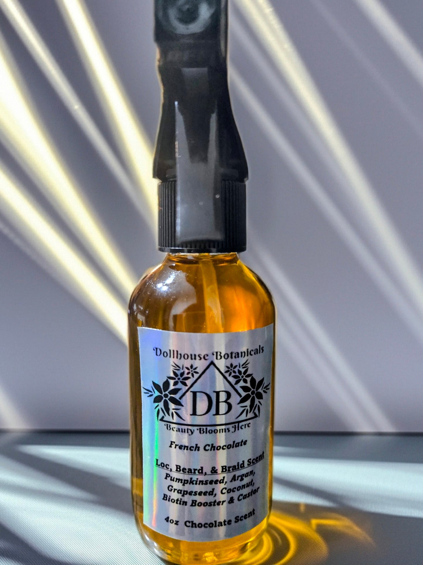  Bottle of Dollhouse Botanicals French Chocolate Loc, Beard, and Braid Scent. Golden oil in glass bottle with trigger sprayer. Front facing with label and ingredients displayed. Unisex hair scent.