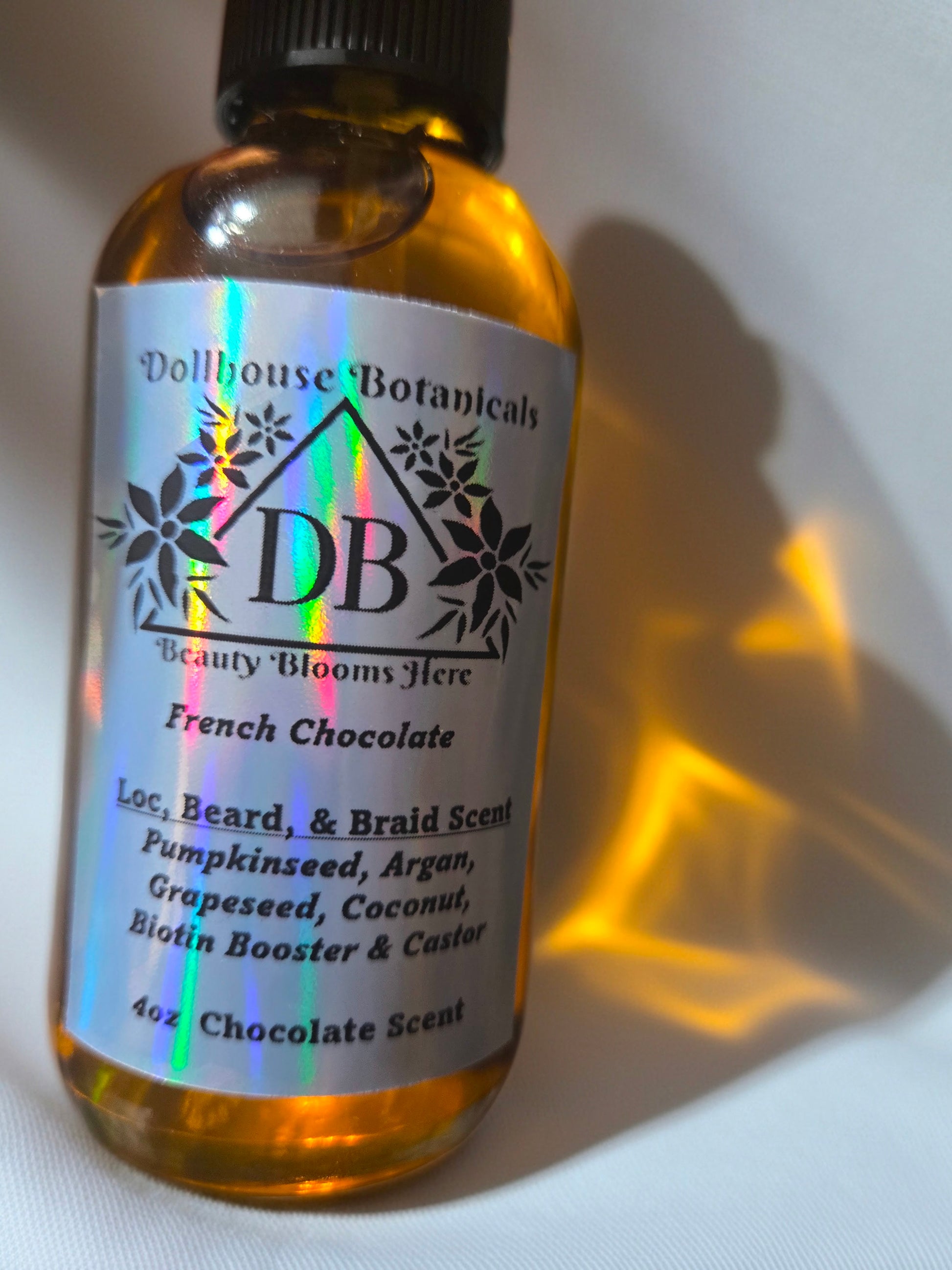 Bottle of Dollhouse Botanicals French Chocolate Loc, Beard, and Braid Scent. Golden oil in glass bottle. Front facing with label and ingredients displayed. Unisex hair scent.