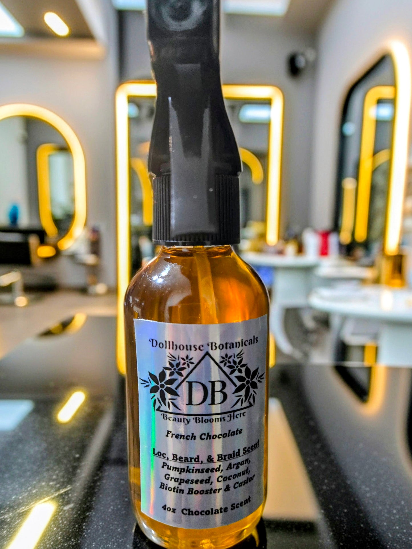  Bottle of Dollhouse Botanicals French Chocolate Loc, Beard, and Braid Scent. Golden oil in glass bottle with trigger sprayer. Front facing with label and ingredients displayed. Unisex hair scent.