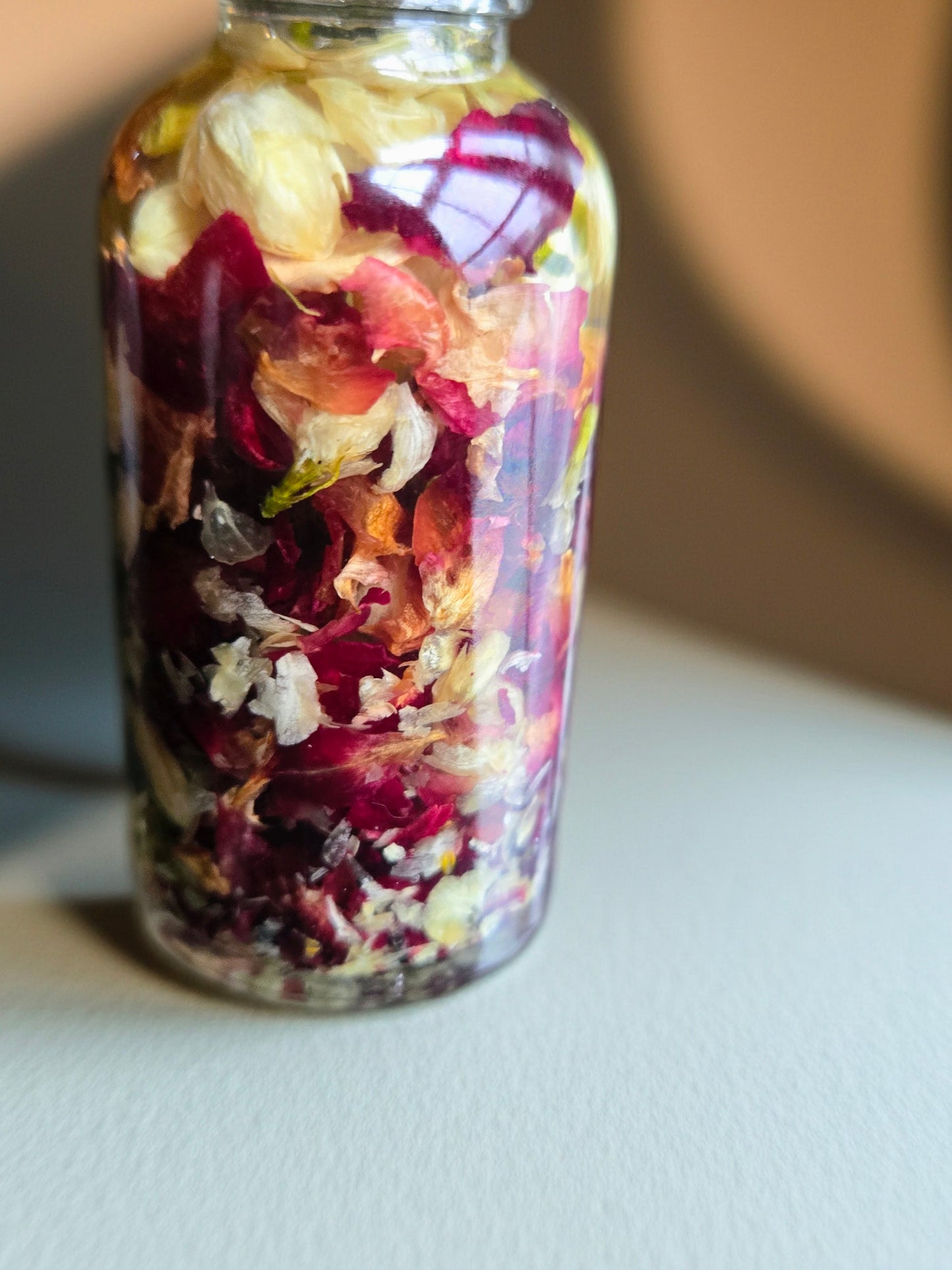 Bottle of Dollhouse Botanicals French Quarter Flora Lip Hydrator. Oil with floating dried rose petals and jasmine petals in glass bottle. Lip moisturizer.
