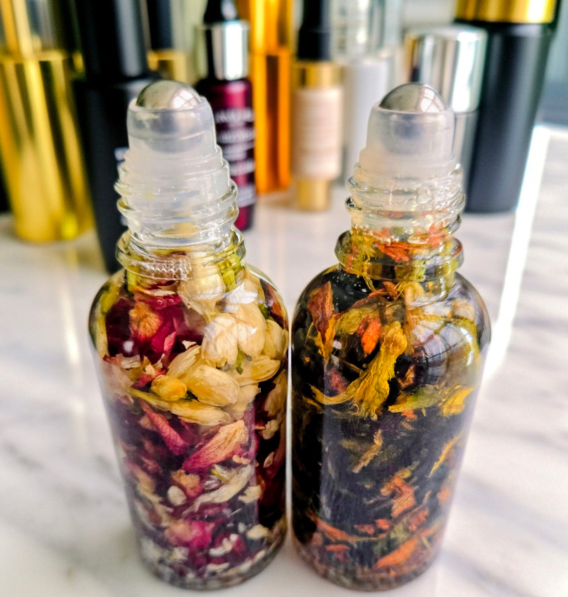 Dollhouse Botanicals French Quarter Lip Hydrator and Dollhouse Botanicals Mermaid Water Lip Hydrator, side by side. Oils with floating flora in glass bottles. Lip moisturizers.