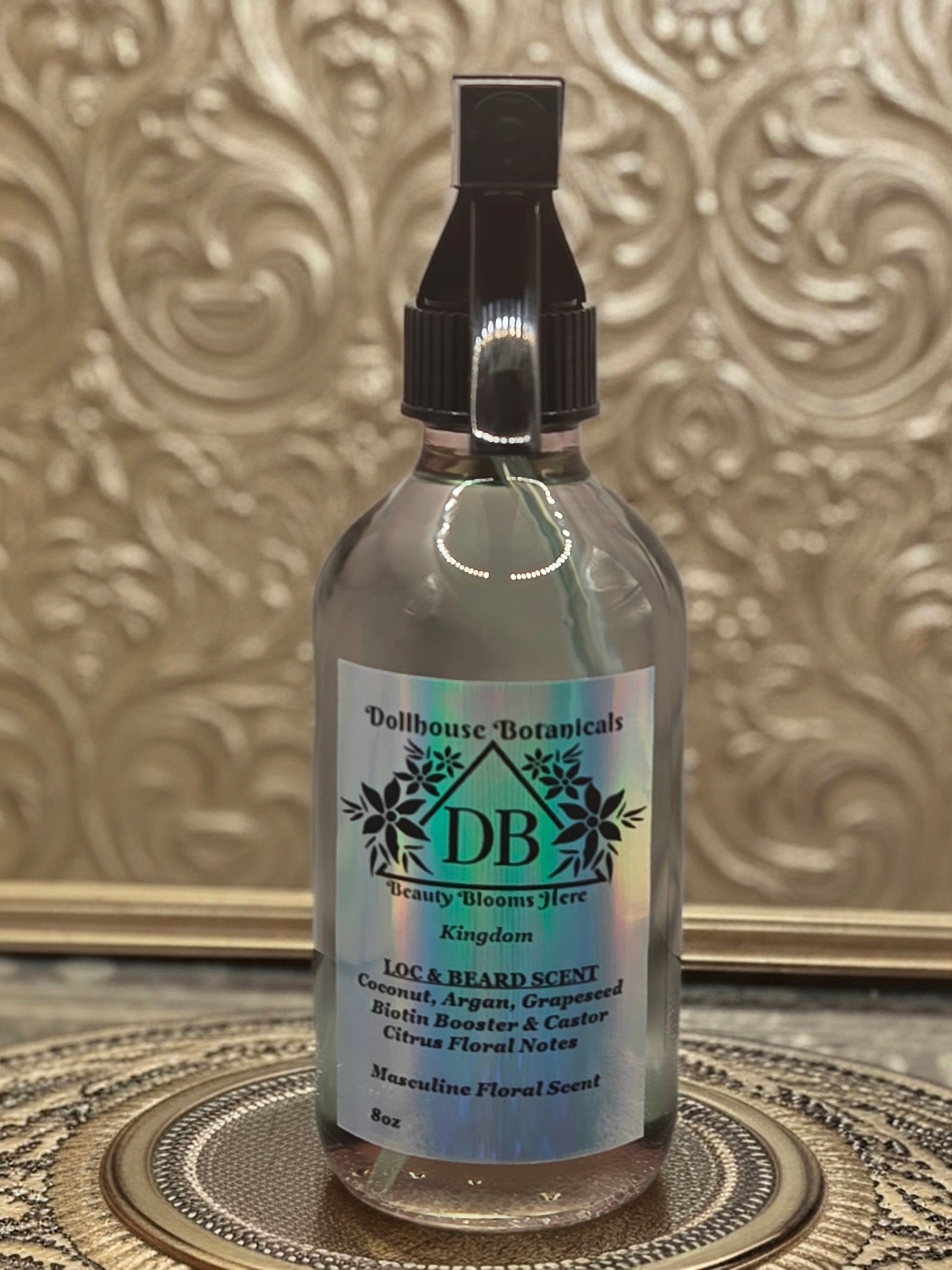 Bottle of Dollhouse Botanicals Kingdom Loc and Beard Scent. Oil in glass bottle with trigger sprayer. Front facing with label and ingredients displayed.