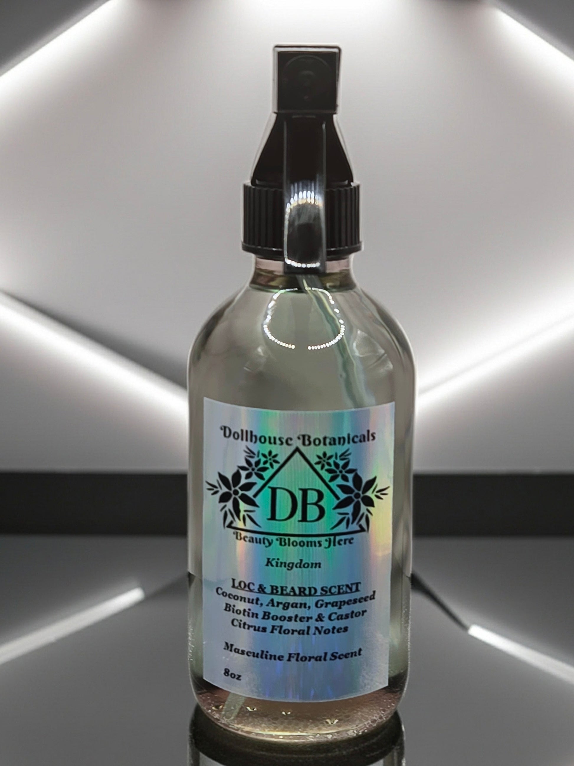 Bottle of Dollhouse Botanicals Kingdom Loc and Beard Scent. Oil in glass bottle with trigger sprayer. Front facing with label and ingredients displayed.