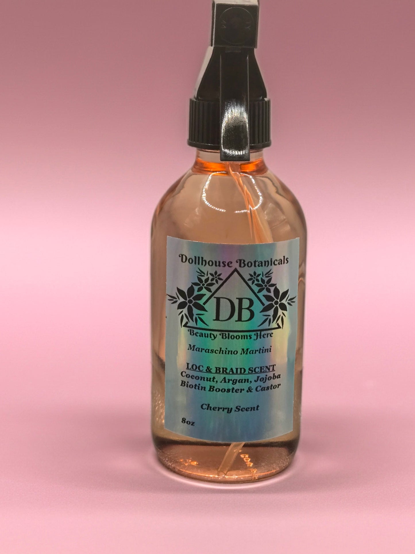Bottle of Dollhouse Botanicals Maraschino Martini Loc and Braid Scent. Oil in glass bottle with trigger sprayer. Feminine hair fragrance. Front facing with ingredients displayed.