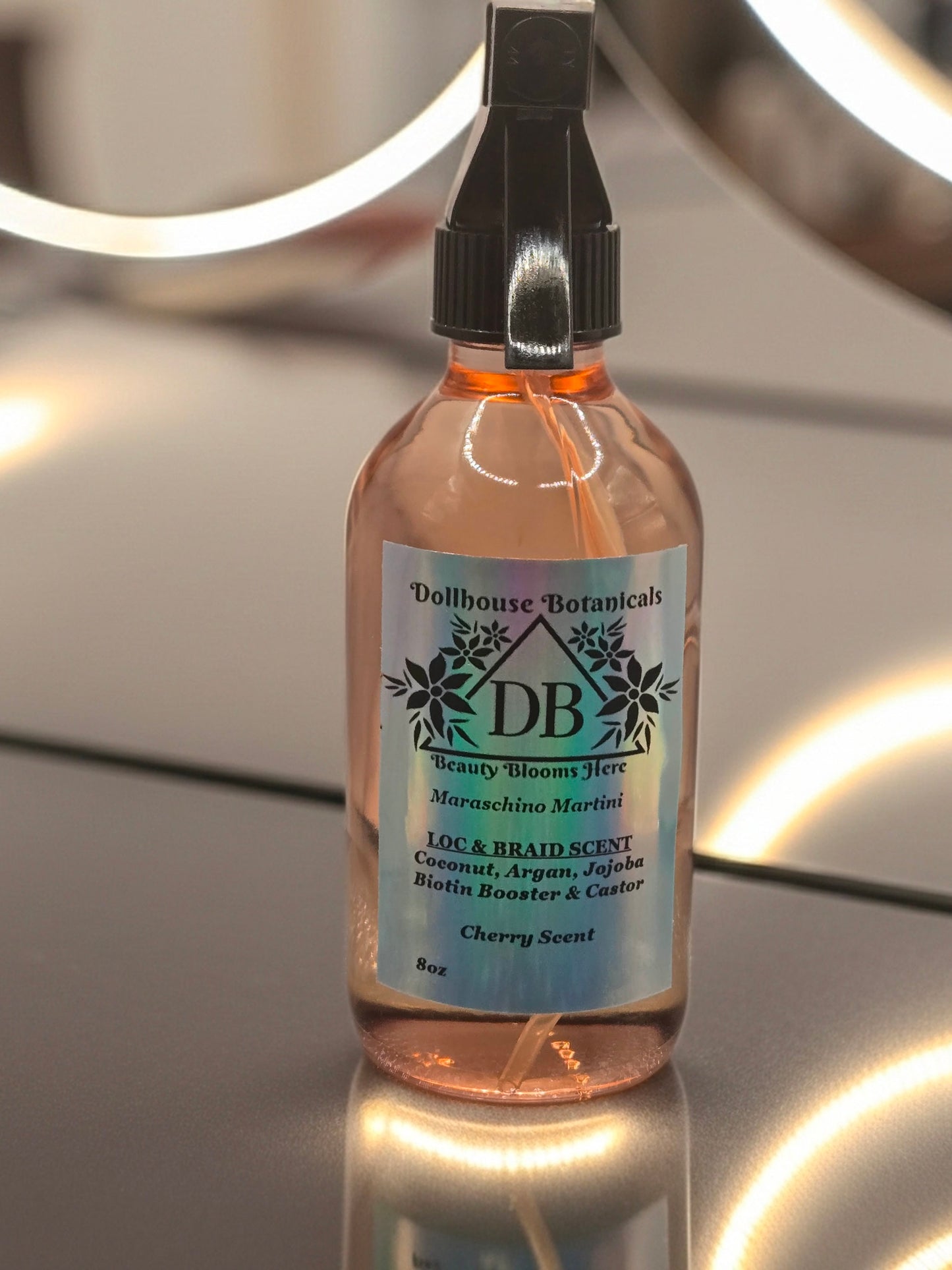Bottle of Dollhouse Botanicals Maraschino Martini Loc and Braid Scent. Oil in glass bottle with trigger sprayer. Feminine hair fragrance. Front facing with ingredients displayed.