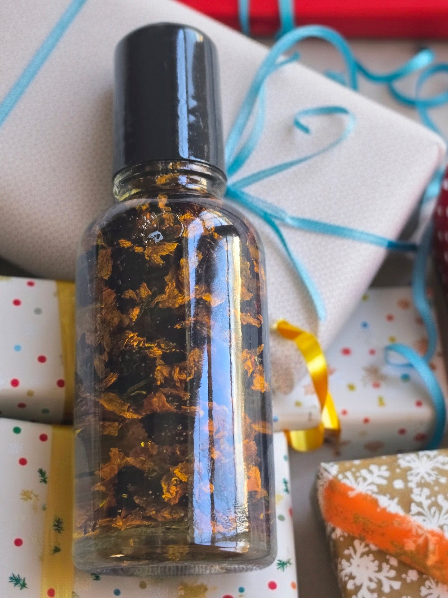 Bottle of Dollhouse Botanicals Moonlight Flora Face Hydrator. Golden oil with floating dried snow chrysanthemum in glass bottle with black top.
