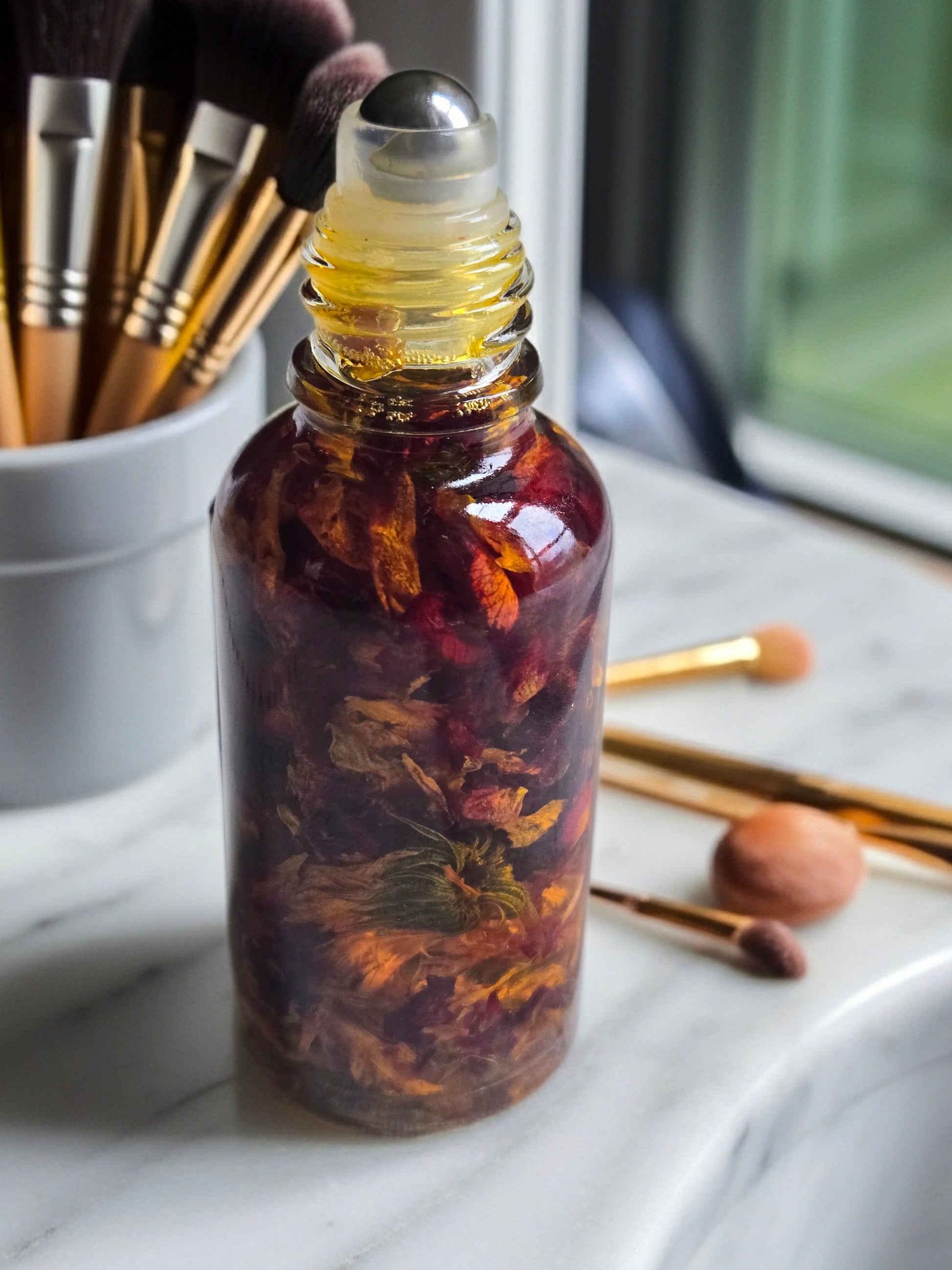 Bottle of Dollhouse Botanicals Red Sea Flora Face Hydrator. Oil with floating calendula and rose petals in glass bottle with steel roller ball applicator.