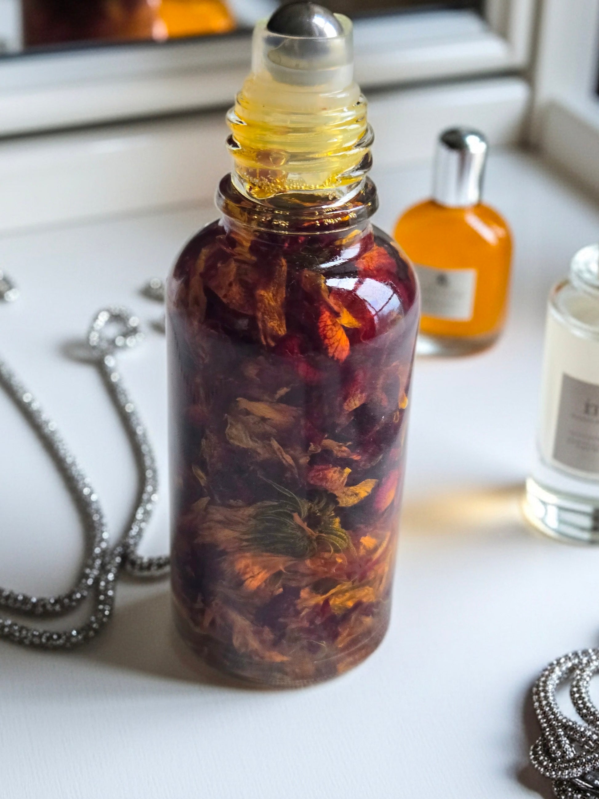 Bottle of Dollhouse Botanicals Red Sea Flora Face Hydrator. Oil with floating calendula and rose petals in glass bottle with steel roller ball applicator.