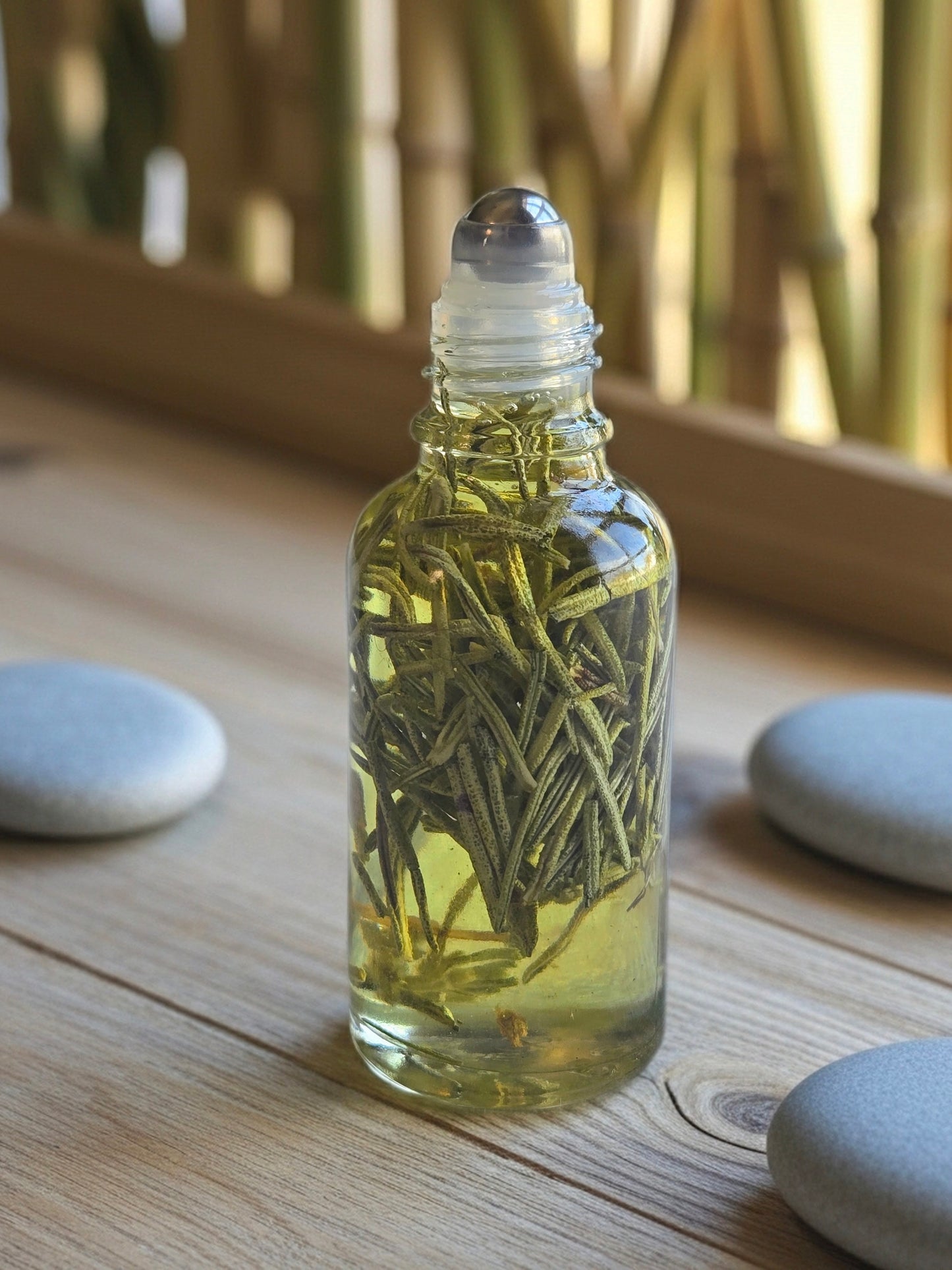 Bottle of Dollhouse Botanicals Bottle of Rosemary's Lavender Flora Face Hydrator. Oil with floating rosemary in glass bottle with steel roller ball applicator, in spa background.