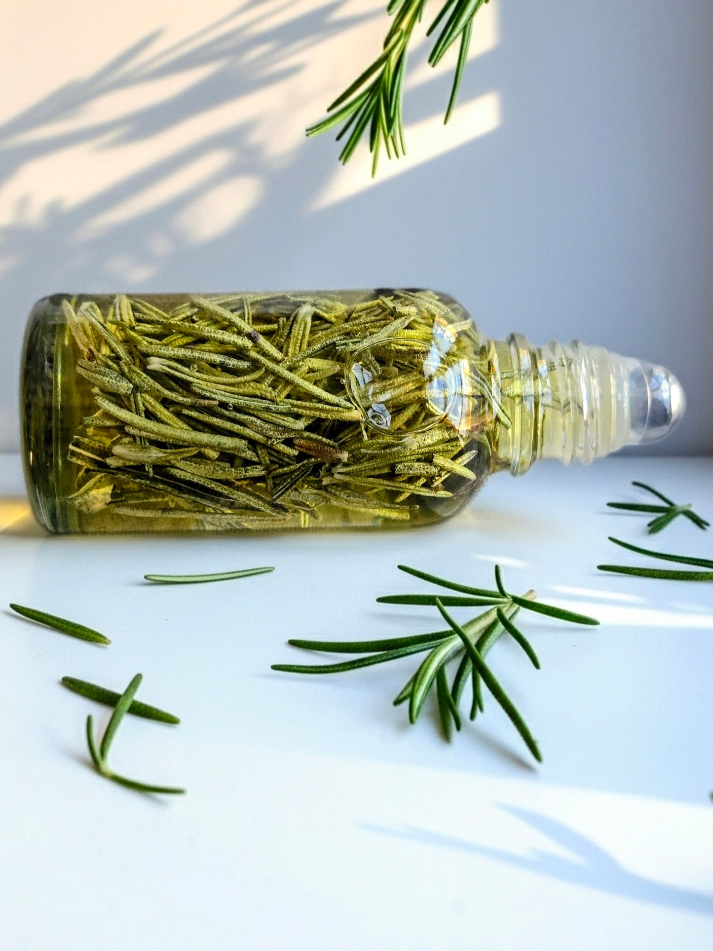 Bottle of Dollhouse Botanicals Rosemary's Lavender Flora Face Hydrator. Oil with floating rosemary in glass bottle with steel roller ball applicator.