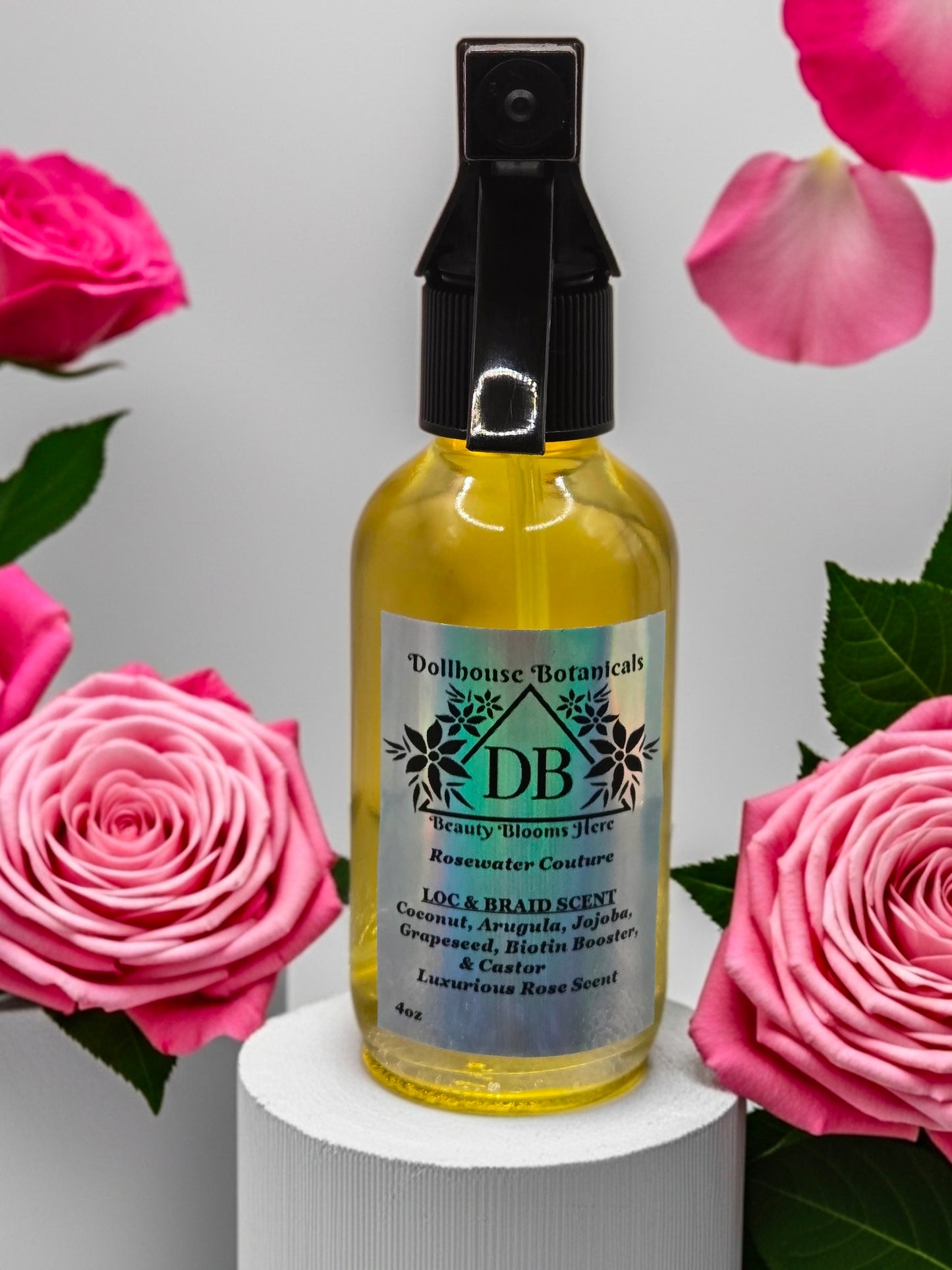 Bottle of Dollhouse Botanicals Rosewater Couture Loc and Braid Scent. Golden oil in clear glass bottle with black trigger sprayer applicator.