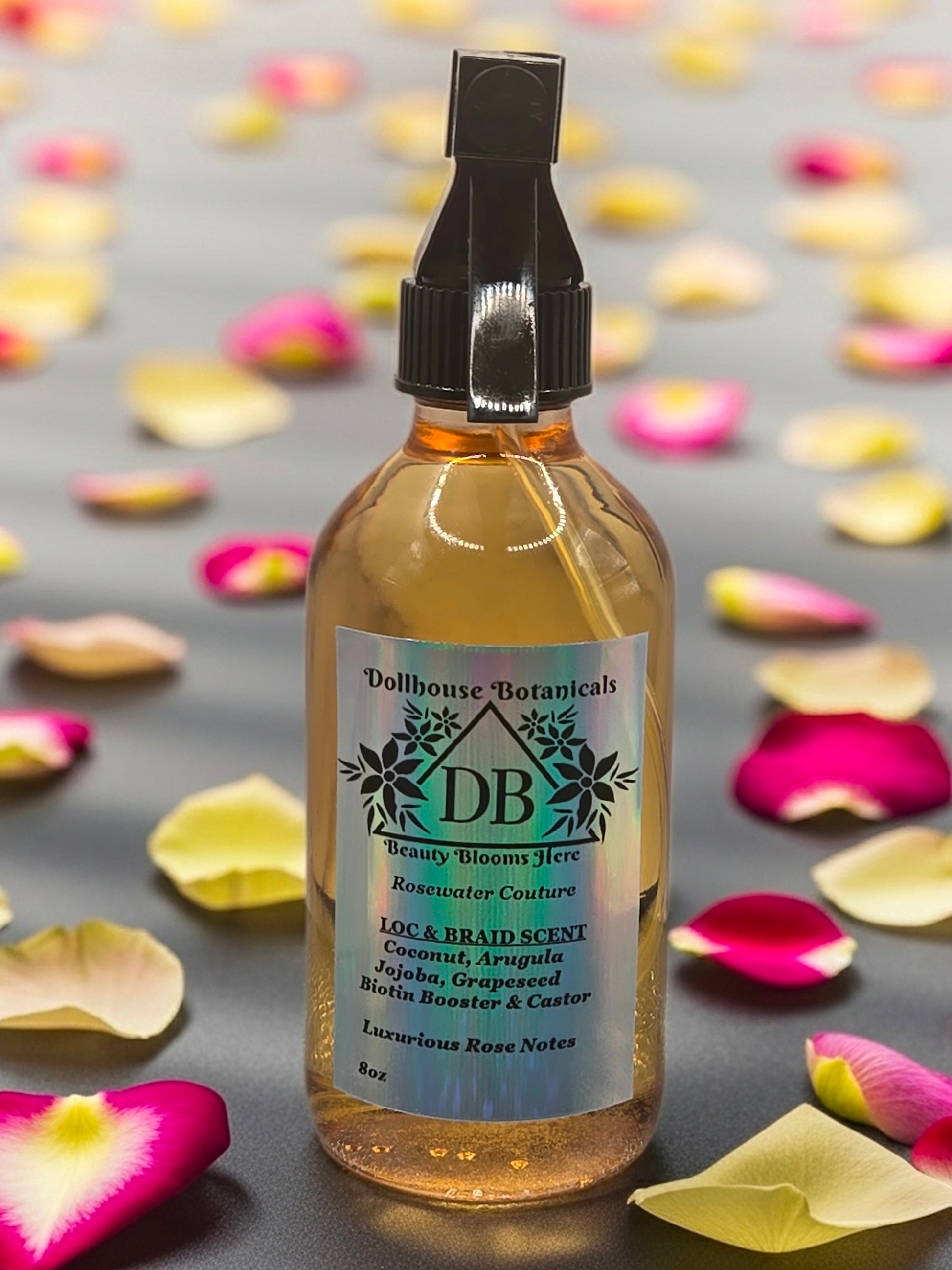 Bottle of Dollhouse Botanicals Rosewater Couture Loc and Braid Scent. Golden oil in glass bottle with trigger sprayer. Front facing with label and ingredients displayed.