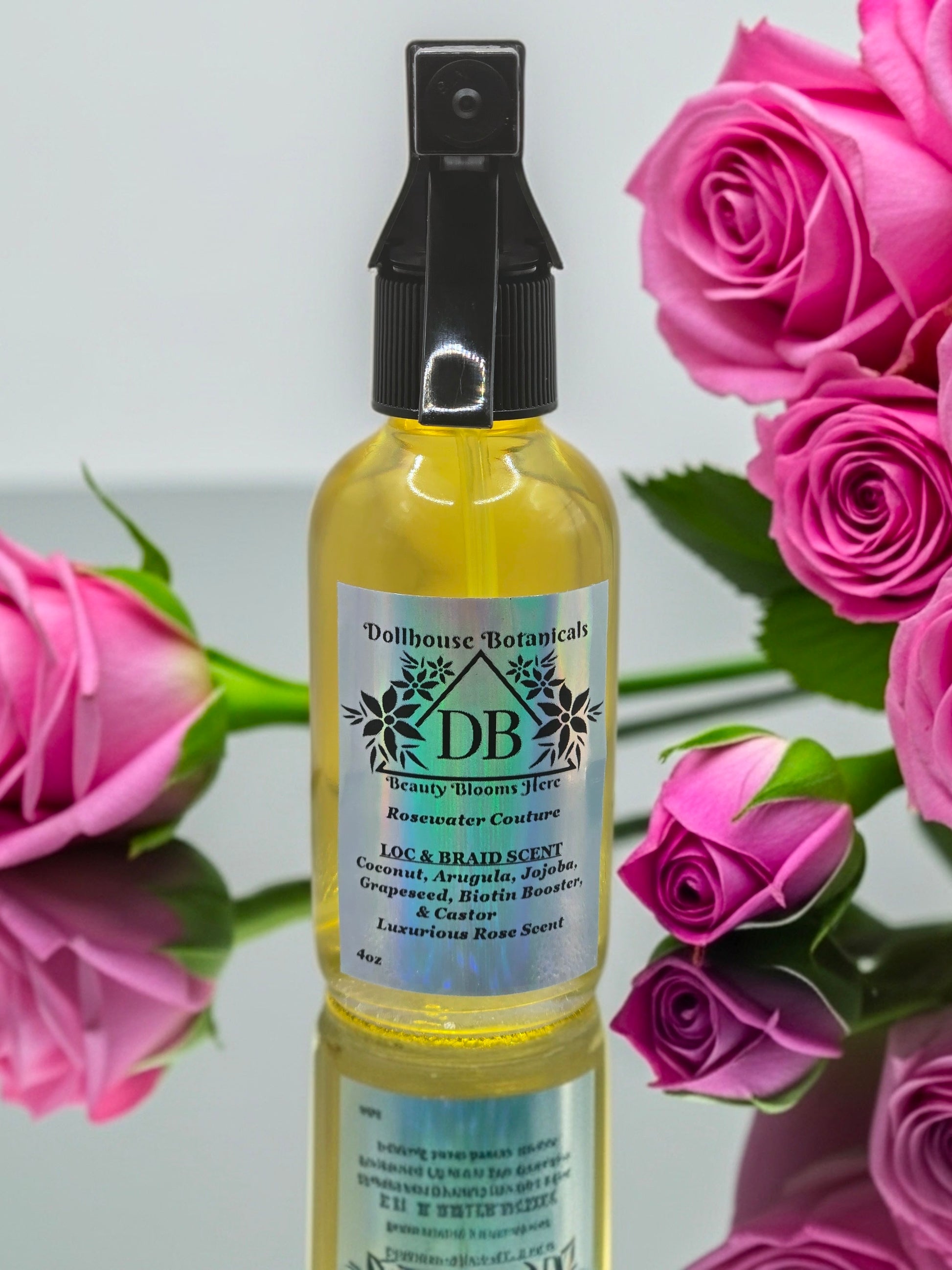 Bottle of Dollhouse Botanicals Rosewater Couture Loc and Braid Scent. Golden oil in clear bottle with black trigger sprayer applicator.