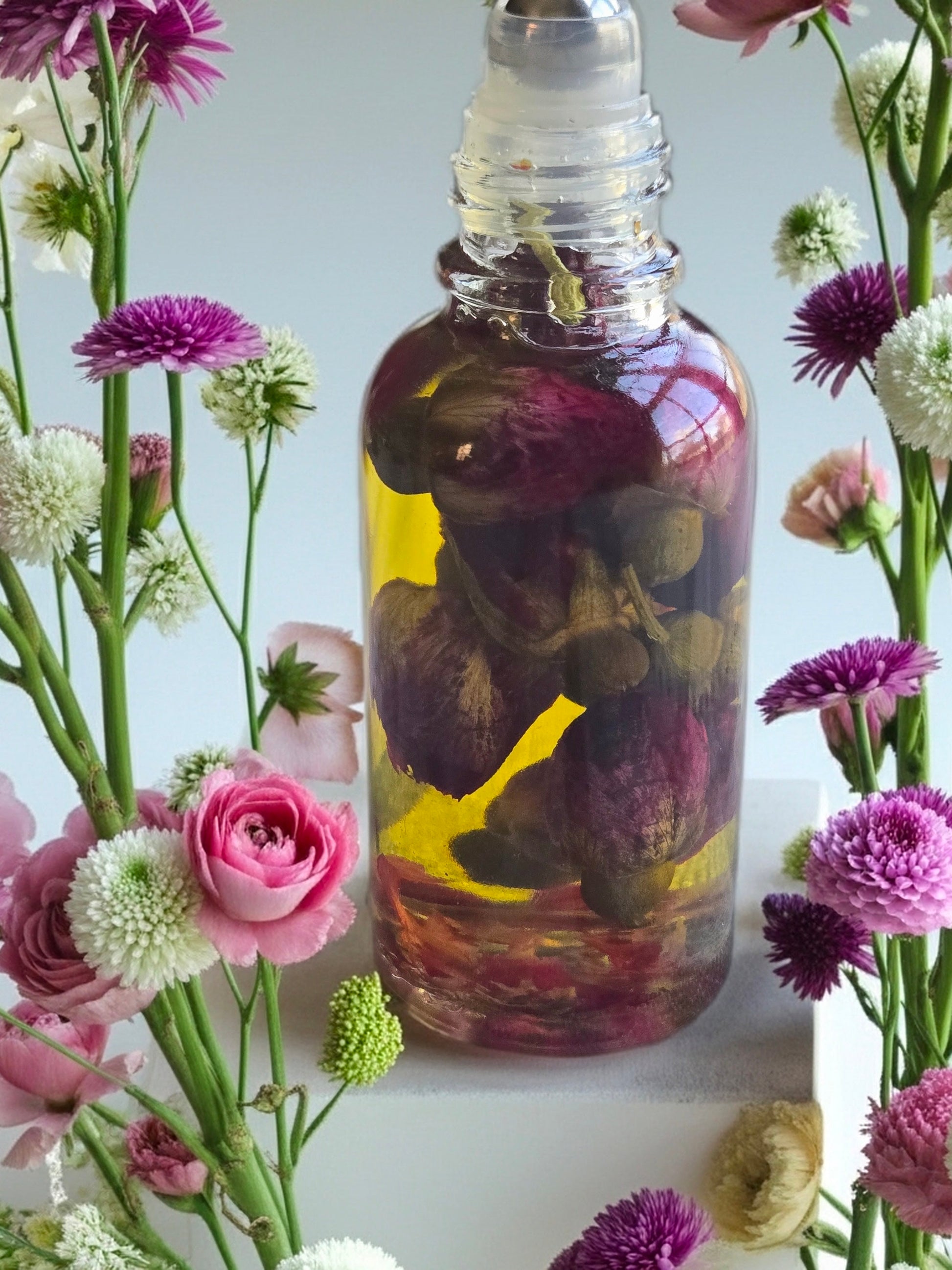 Bottle of Dollhouse Botanicals White Wine Flora Face Hydrator. Floating rose buds floating in golden oil in glass bottle with steel roller ball.