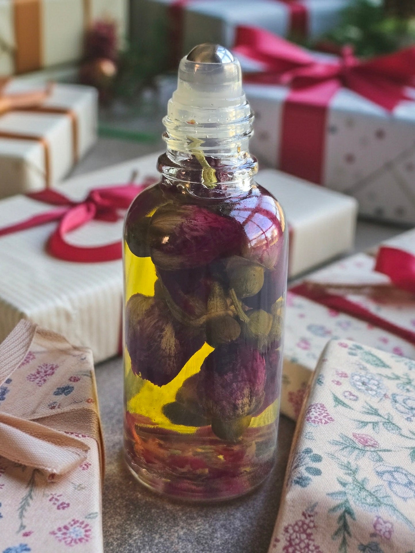 Bottle of Dollhouse Botanicals White Wine Flora Face Hydrator. Golden oil with floating dried rose buds in glass bottle with steel roller ball applicator.