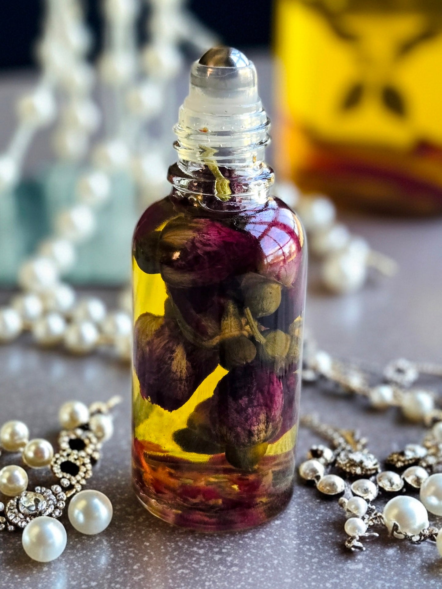 Bottle of Dollhouse Botanicals White Wine Flora Face Hydrator with Squalane and Chia Seed. Golden oil with floating dried rose buds in glass bottle with steel roller ball applicator.