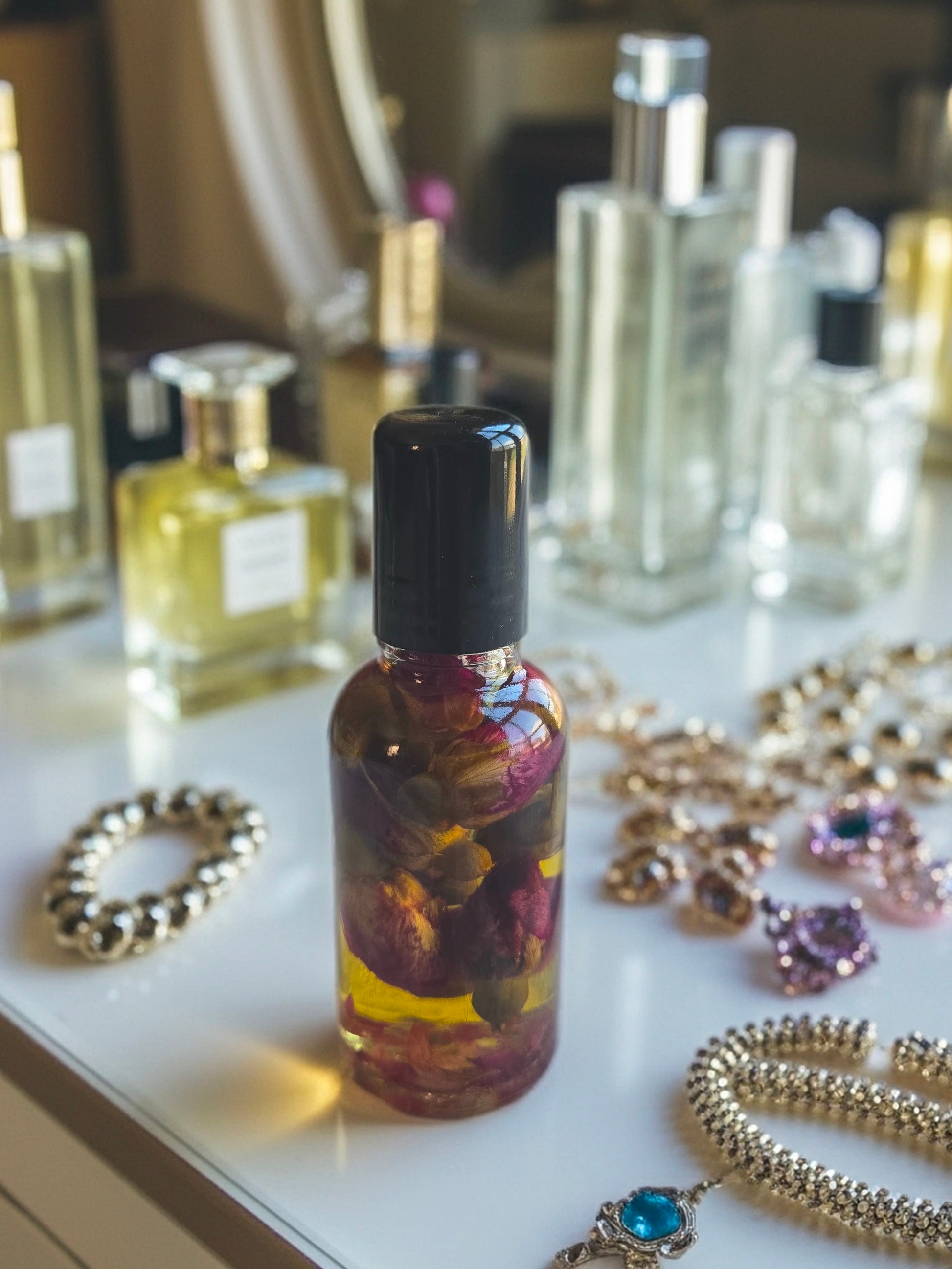 Bottle of Dollhouse Botanicals White Wine Flora Face Hydrator. Golden oil with floating dried rose buds in glass bottle with black top.
