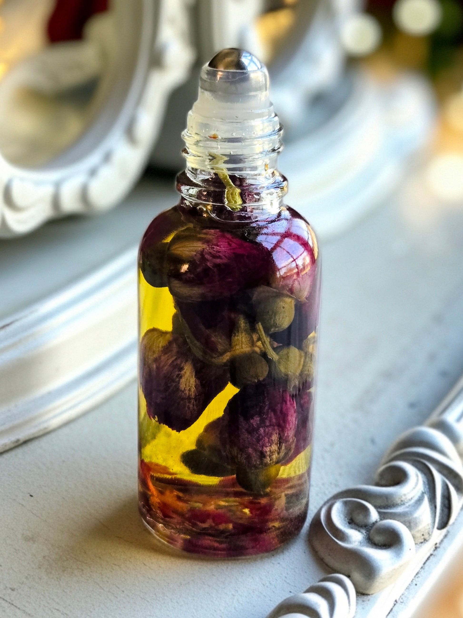 Bottle of Dollhouse Botanicals White Wine Flora Face Hydrator. Golden oil with floating dried rose buds in glass bottle with steel roller ball applicator.