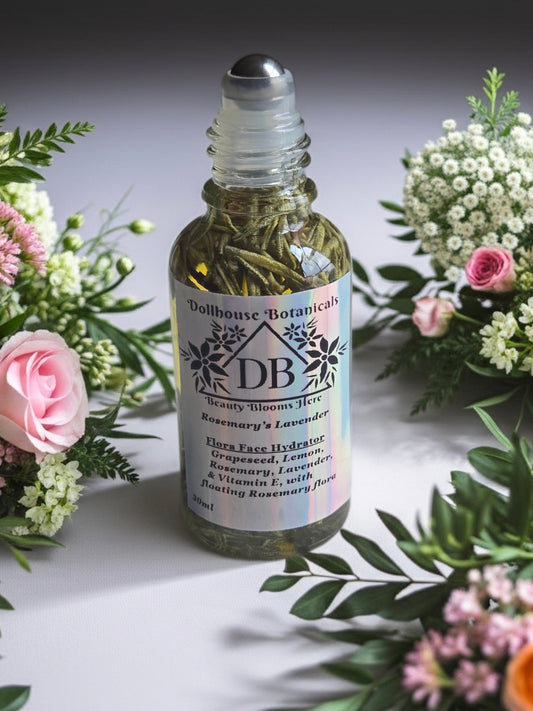 Bottle of Dollhouse Botanicals Rosemary's Lavender Flora Face Hydrator with steel roll on applicator, sitting on white surface with flowers.