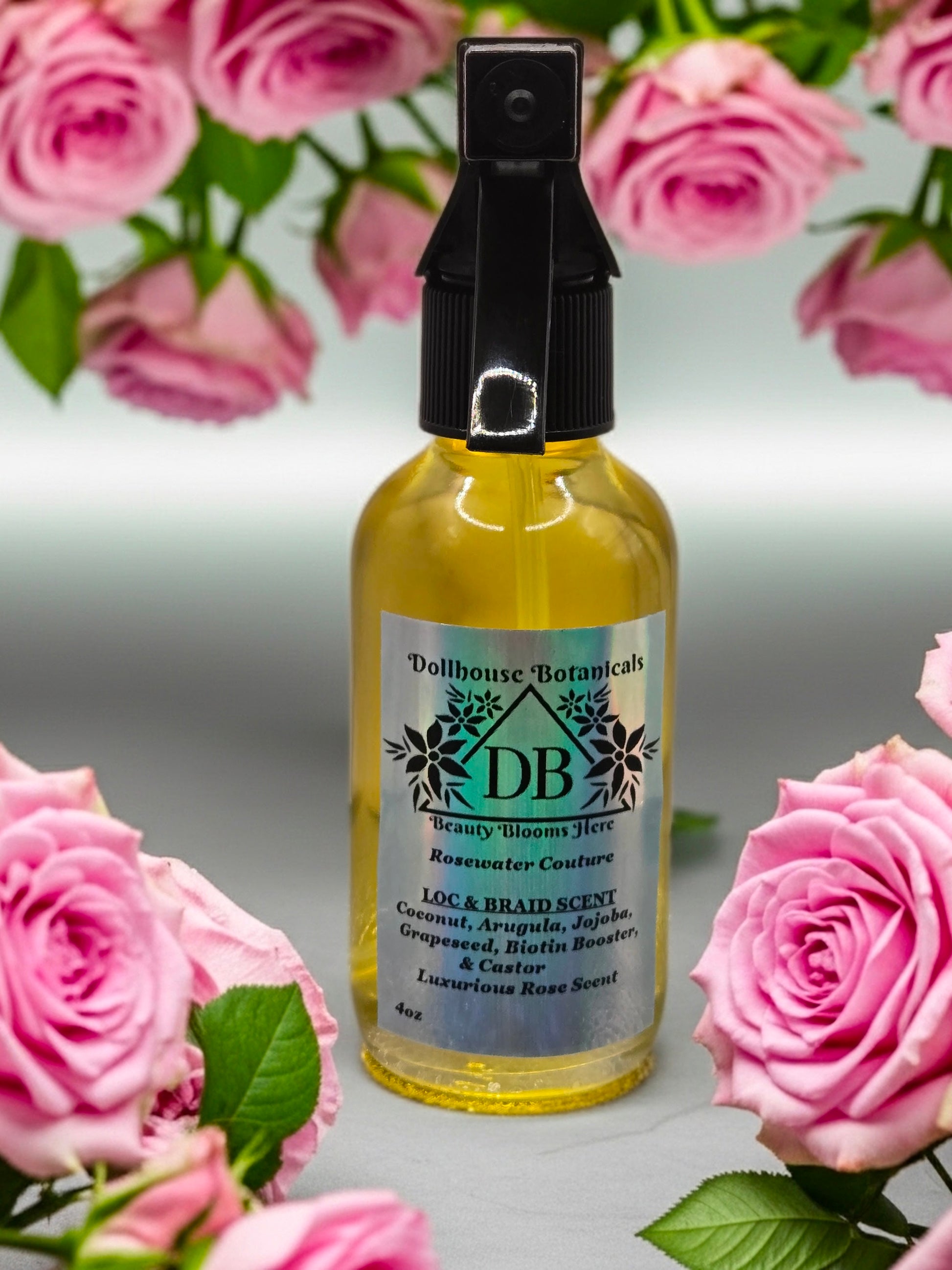 Bottle of Dollhouse Botanicals Rosewater Couture Loc and Braid Scent. Gold oil in clear bottle with black trigger sprayer applicator.